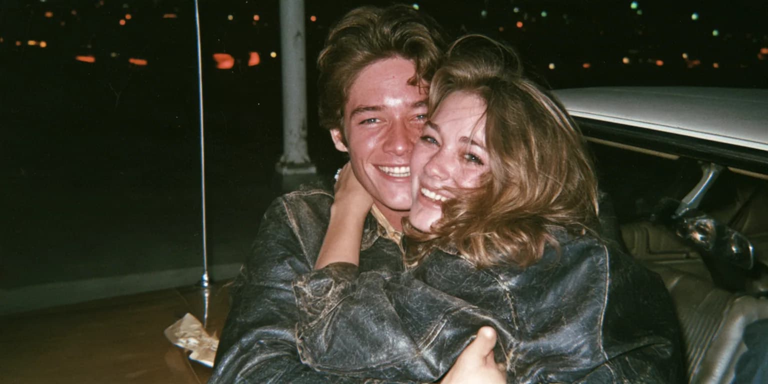 Night-time flash photo of a laughing teenage couple hugging beside a 1960s car, made with Midjourney V8.2
